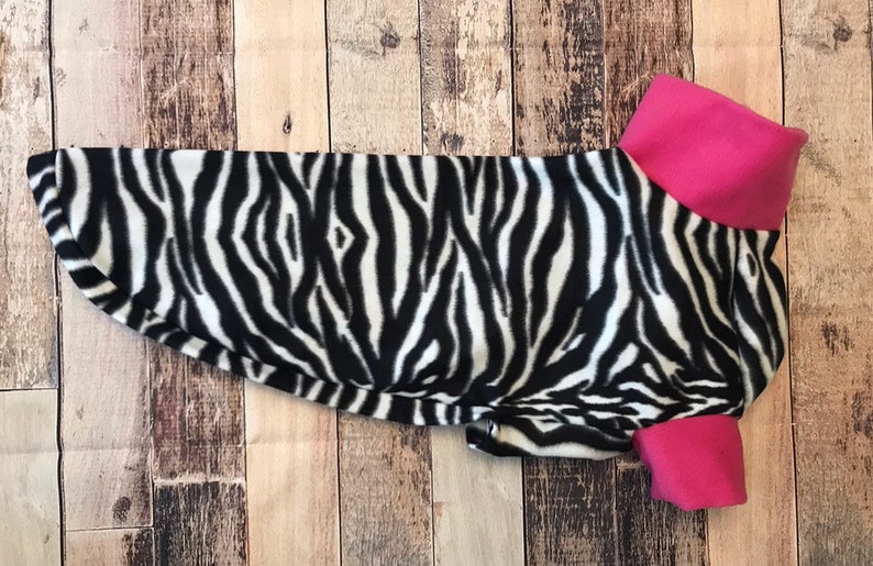 May include: A black and white zebra print dog sweater with a pink collar.