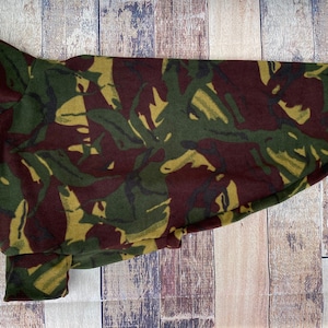 Op de afbeelding: Een camouflage-gepatroneerde hondentrui met een hoge hals en een lang, vloeiend ontwerp. De trui is gemaakt van een zachte, comfortabele stof en heeft een bruin, groen en geel kleurenschema.