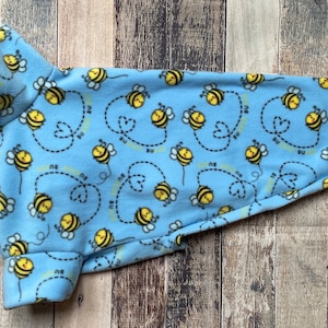 Op de afbeelding: Een lichtblauwe fleece hondentrui met een patroon van gele bijen die in een hartvorm vliegen. De trui heeft een rolkraag.