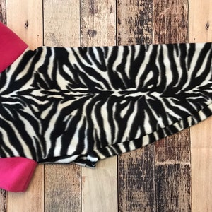 May include: A black and white zebra print dog shirt with pink trim around the collar and sleeves.