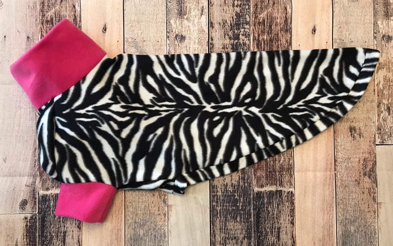 May include: A black and white zebra print dog shirt with pink trim around the collar and sleeves.