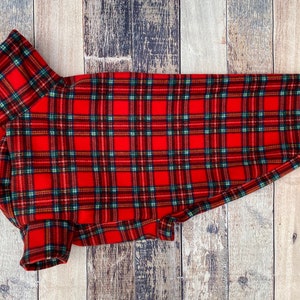 Op de afbeelding: Rood en groen geruite hondenjas. De jas heeft een klassiek tartanpatroon met een rode basis en groene, blauwe en gele accenten. De jas is ontworpen voor een hond en heeft een coltrui.