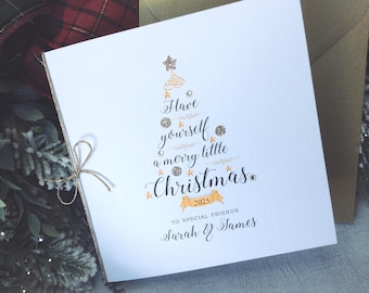 May include: A white Christmas card with a gold glitter tree design. The card features the text "Have yourself a merry little Christmas" with the year 2025. The card is addressed to "Special Friends" Sarah & James.