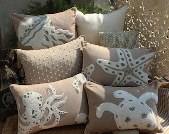 May include: A collection of rectangular throw pillows in beige fabric featuring white and green beaded marine life designs including an octopus, a starfish, and a sea turtle, alongside a pillow with white dot embroidery and a solid white pillow.
