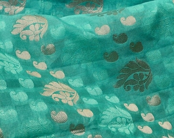 Pode incluir: Tecido turquesa com um padrão floral prateado. O tecido tem um brilho sutil e uma textura macia.