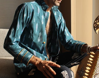 May include: A long-sleeved teal shirt featuring a vertical ikat pattern in white, red, and blue. The shirt has a mandarin collar, a button-down front with visible buttons, and cuffs accented with a thin, decorative yellow and red striped trim.