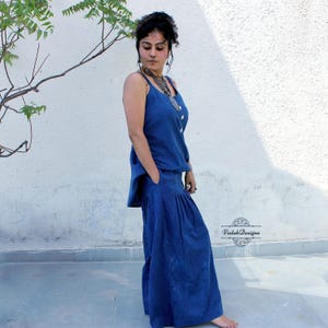 May include: A dark blue sleeveless top and matching wide-leg trousers set featuring a subtle vertical pinstripe pattern. The top has thin shoulder straps and the trousers include side pockets and a pleated waistline. The text Vedah Designs is visible.