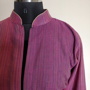 Puede incluir: Una chaqueta de manga larga, de rayas rosa y p&uacute;rpura, con cuello mandar&iacute;n y ribete beige. La chaqueta est&aacute; hecha de una tela ligera y tiene un corte holgado.