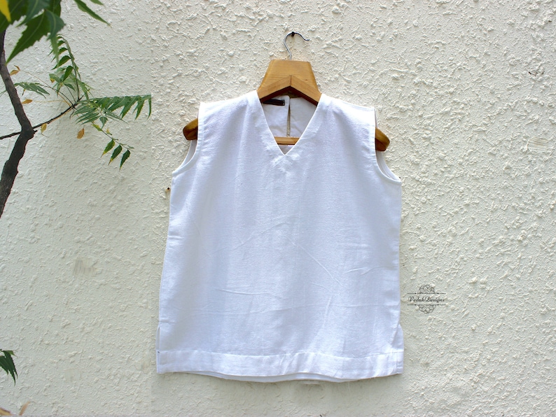 May include: White sleeveless top with a V-neckline and a small label that says "Varda Designs".