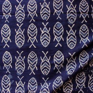 Peut inclure: Un gros plan sur un tissu bleu avec un motif blanc de formes de poissons stylisées. Le tissu est plié et a une texture légèrement froissée.