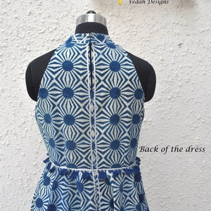 May include: A sleeveless dress featuring a blue and white geometric sunburst pattern, a high neckline, and a vertical zipper closure. The waist is accented with a row of small blue tassels and silver trim. The text Vedah Designs and Back of the dress appear.