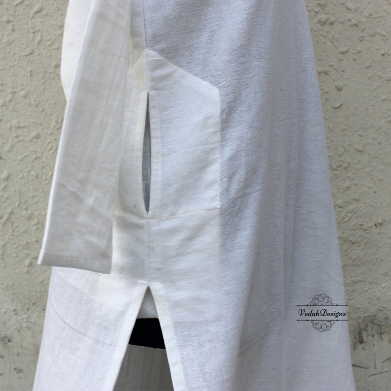 May include: White long-sleeved tunic with a side slit and a pocket on the left side. The tunic is made of a lightweight fabric and has a relaxed fit.