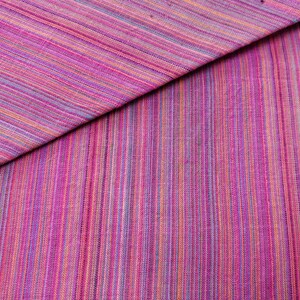 Puede incluir: Primer plano de una tela de rayas rosa y p&uacute;rpura con un brillo sutil. La tela est&aacute; doblada por la mitad, creando una l&iacute;nea diagonal a trav&eacute;s de la imagen.