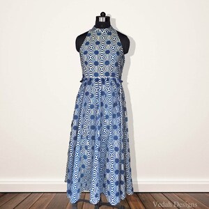 May include: A sleeveless midi dress featuring a high halter neckline and a fitted bodice that transitions into a flared skirt. The fabric is white with a repeating blue geometric sunburst pattern. The text Vedah Designs is visible at the bottom.