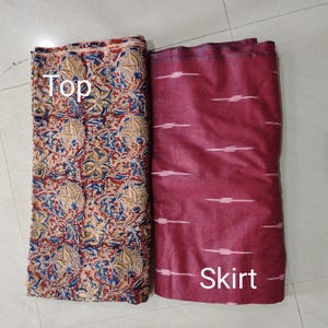 Puede incluir: Dos piezas de tela, una etiquetada como "Top" y la otra como "Skirt". La tela superior tiene un estampado floral rojo, azul y amarillo. La tela de la falda es de color granate con rayas horizontales blancas.
