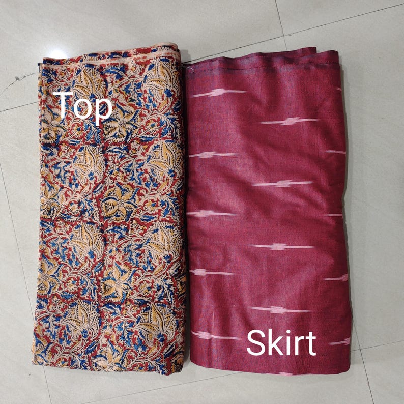 Puede incluir: Dos piezas de tela, una etiquetada como "Top" y la otra como "Skirt". La tela superior tiene un estampado floral rojo, azul y amarillo. La tela de la falda es de color granate con rayas horizontales blancas.