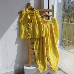Puede incluir: Una blusa amarilla sin mangas y pantalones a juego. La blusa tiene un frente abotonado y los pantalones son holgados.