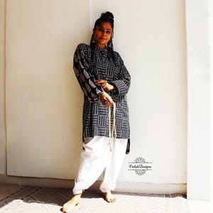 May include: A woman wearing a black and white patterned tunic with long sleeves and white pants. She is holding a string of beads in her hand. The text "Vardah Designs" is visible in the lower right corner of the image.