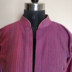 Puede incluir: Una chaqueta de manga larga a rayas rosa y blancas con cuello mandar&iacute;n.