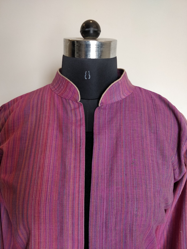 Puede incluir: Una chaqueta de manga larga a rayas rosa y blancas con cuello mandar&iacute;n.