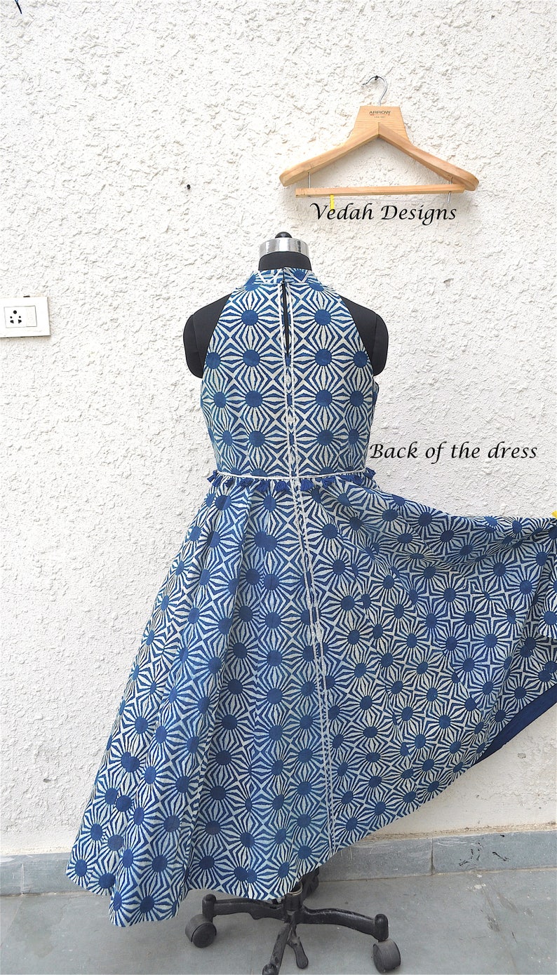 May include: A sleeveless dress featuring a blue and white geometric sunburst pattern, a high halter neckline, and a central vertical seam. The garment is displayed on a mannequin, with the text Vedah Designs and Back of the dress visible.