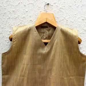 May include: A sleeveless, light brown vest with a V-neckline. The vest is made of a textured fabric and has a subtle sheen.