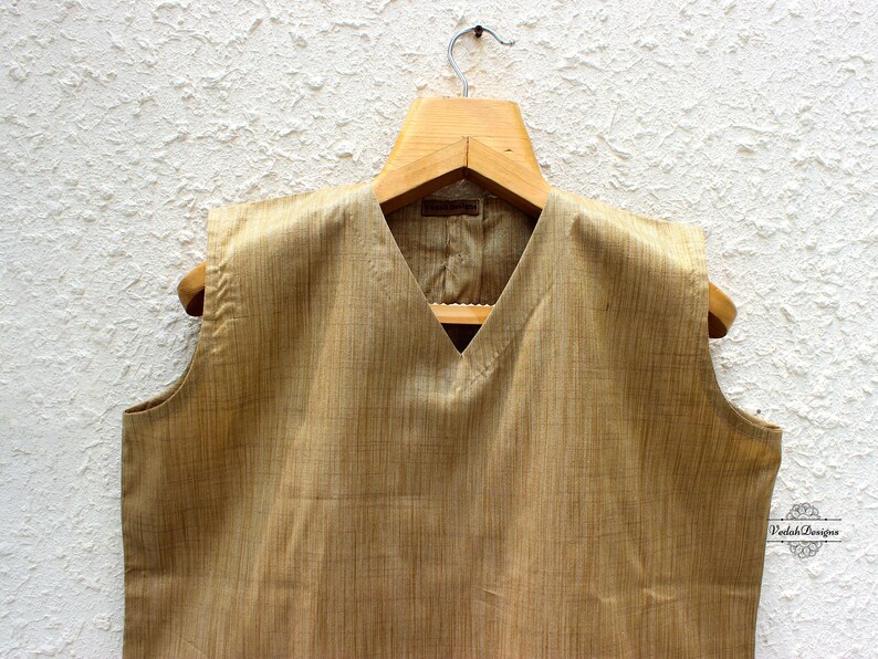May include: A sleeveless, light brown vest with a V-neckline. The vest is made of a textured fabric and has a subtle sheen.