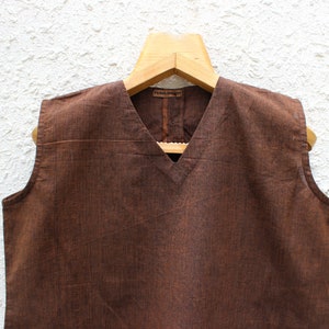 May include: A brown sleeveless top with a V-neckline. The top is made of a textured fabric and has a simple design.