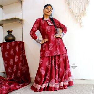 May include: A red and white paisley print long-sleeved top and skirt set. The top has a mandarin collar and a button closure. The skirt is a-line and has a white trim.