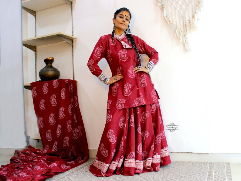 May include: A red and white paisley print long-sleeved top and skirt set. The top has a mandarin collar and a button closure. The skirt is a-line and has a white trim.