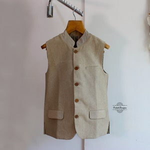 May include: A beige sleeveless waistcoat with a button-up front and pockets. The waistcoat is made of a textured fabric and has a simple design.