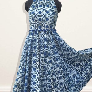 May include: A sleeveless midi dress featuring a high neckline and a flared skirt. The garment is decorated with a repeating blue and white geometric sunburst pattern. A thin waistband with small blue tassels separates the bodice from the skirt.