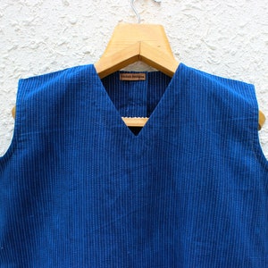 May include: A sleeveless blue cotton top with white stripes and a V-neck. The top has a small label that says "Vedah Designs".