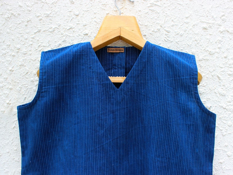 May include: A sleeveless blue cotton top with white stripes and a V-neck. The top has a small label that says "Vedah Designs".