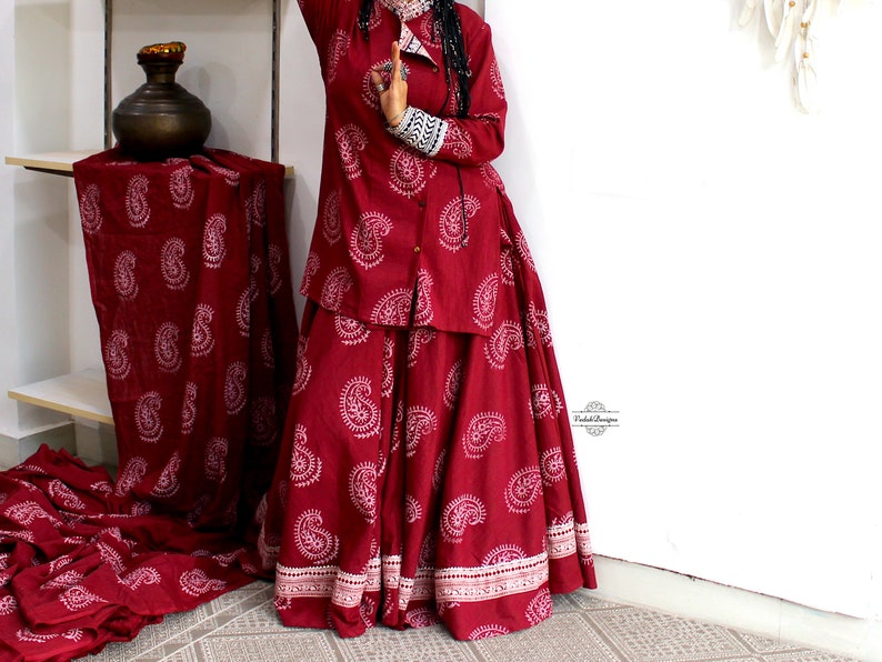 May include: A maroon-colored, long-sleeved shirt and skirt set with a paisley print. The shirt has a button-up front and the skirt is full-length.
