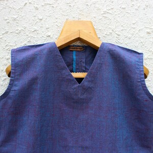 May include: A sleeveless blue cotton top with a V-neckline. The top has a subtle woven pattern and a blue trim around the neckline.