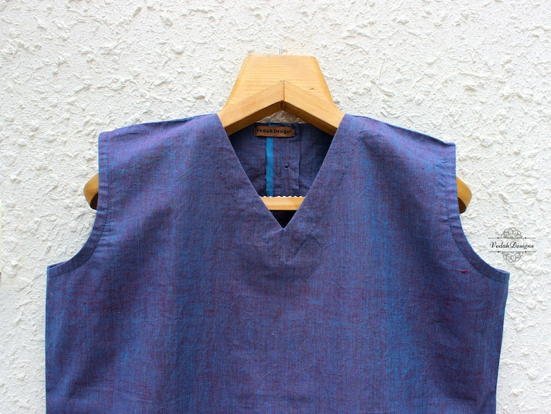 May include: A sleeveless blue cotton top with a V-neckline. The top has a subtle woven pattern and a blue trim around the neckline.