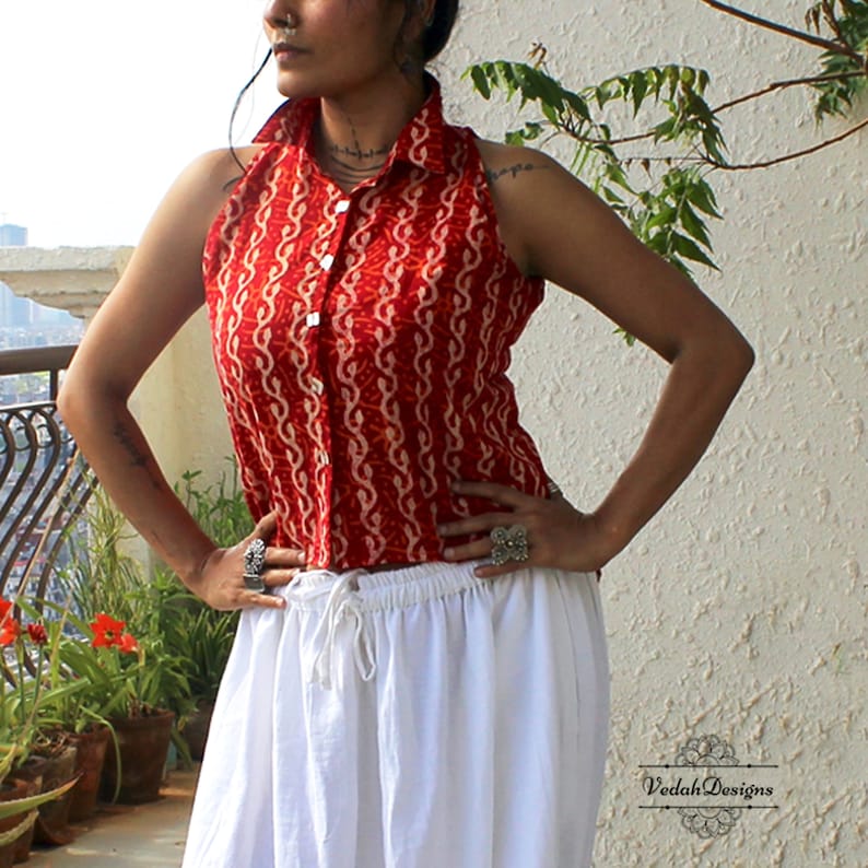 May include: A sleeveless red collared shirt featuring a white vertical wavy pattern and a front button closure, paired with a white skirt that has an elastic waistband with a drawstring. The text VedahDesigns is visible in the bottom right corner.