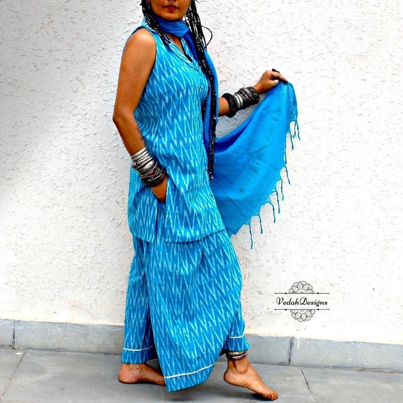 K&ouml;nnte beinhalten: Ein &auml;rmelloses blaues und wei&szlig;es Ikat-Oberteil mit einer passenden Hose. Das Oberteil hat einen Kragen und einen Knopfverschluss. Das Outfit wird mit einem blauen Schal und silbernen Armreifen kombiniert.