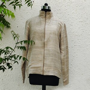 May include: A long-sleeved jacket in a light tan and beige textured fabric with a visible horizontal weave pattern. The jacket features a high collar, a full-length front zipper closure, and straight sleeves, displayed on a black mannequin torso.