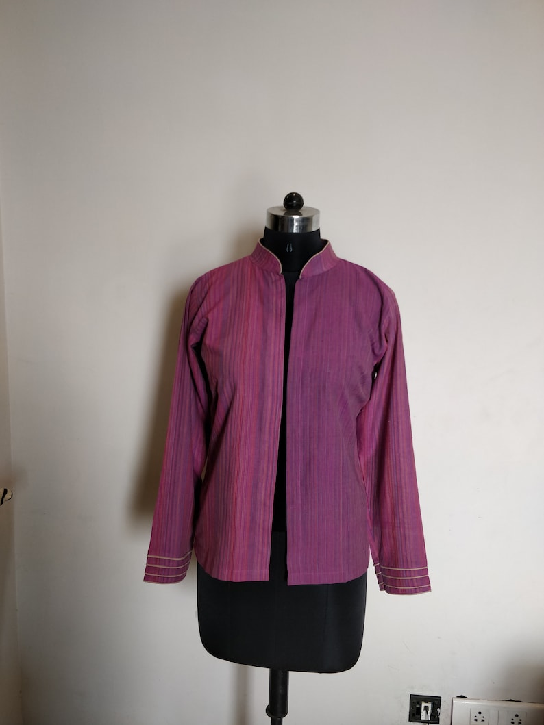 Puede incluir: Una chaqueta de manga larga, de rayas moradas y rosas, con cuello mandar&iacute;n y abertura frontal. La chaqueta tiene un brillo sutil y est&aacute; ribeteada con un fino borde de color crema.