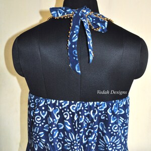 May include: A blue and white patterned halter dress displayed on a black mannequin. The dress features a bow at the neck with gold bead accents. The fabric has a floral and abstract design. The text "Veda Designs" is visible.