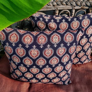 May include: Two decorative throw pillows with a dark blue background and a white and red paisley pattern. The pillows are sitting on a brown surface.
