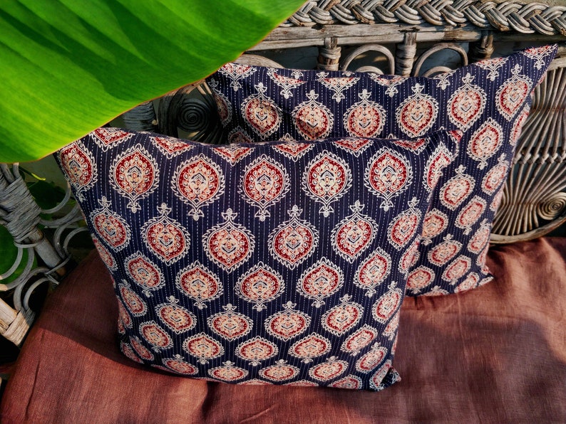 May include: Two decorative throw pillows with a dark blue background and a white and red paisley pattern. The pillows are sitting on a brown surface.