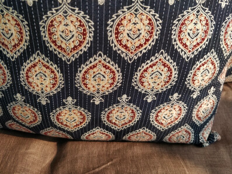 May include: A dark blue throw pillow with a white and brown paisley pattern. The pillow is quilted with white stitching.