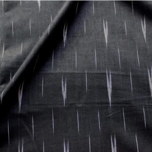 May include: A dark charcoal gray fabric featuring a repeating pattern of thin, vertical white dashes. The textile displays a woven texture with a subtle, irregular ikat-style design where the white lines appear slightly blurred and elongated.