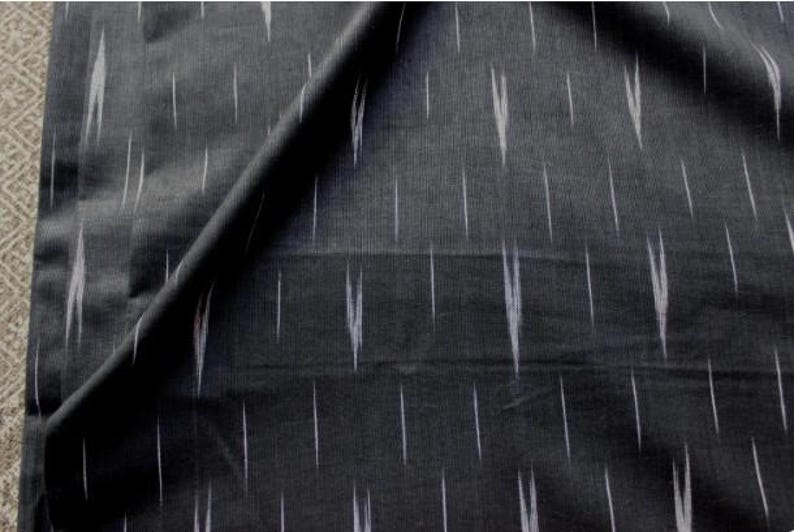 May include: A dark charcoal gray fabric featuring a repeating pattern of thin, vertical white dashes. The textile displays a woven texture with a subtle, irregular ikat-style design where the white lines appear slightly blurred and elongated.