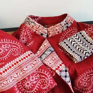 May include: A red cotton jacket with a white and black paisley print. The jacket has a mandarin collar and long sleeves with white and black trim. The jacket is made in India.
