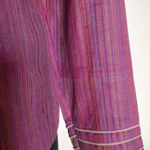 Puede incluir: Una camisa de manga larga con un patr&oacute;n a rayas en tonos de rosa, morado, azul y naranja. La camisa tiene un ribete blanco alrededor de los pu&ntilde;os.