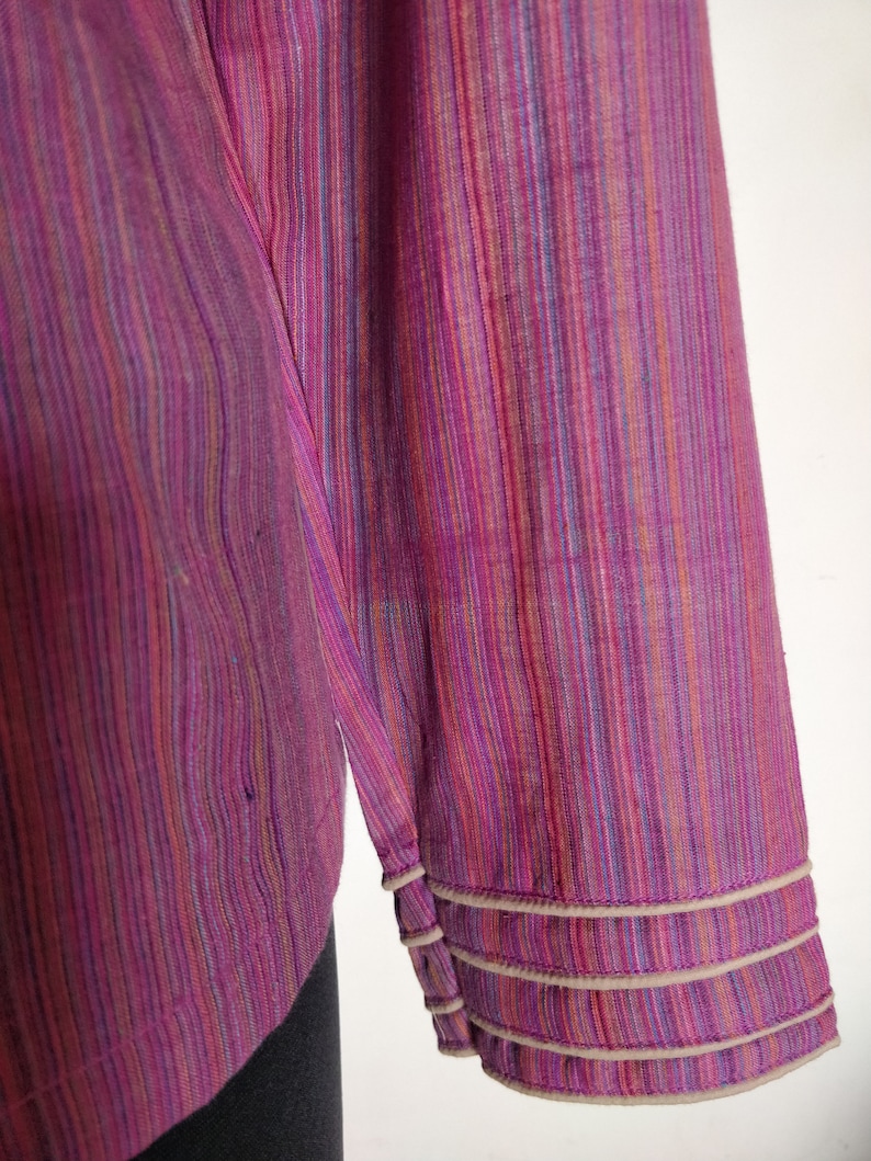 Puede incluir: Una camisa de manga larga con un patr&oacute;n a rayas en tonos de rosa, morado, azul y naranja. La camisa tiene un ribete blanco alrededor de los pu&ntilde;os.